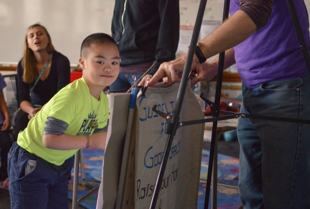 Young Upstream Arts participant standing in front of an easel, looking at the camera, and ready to paint